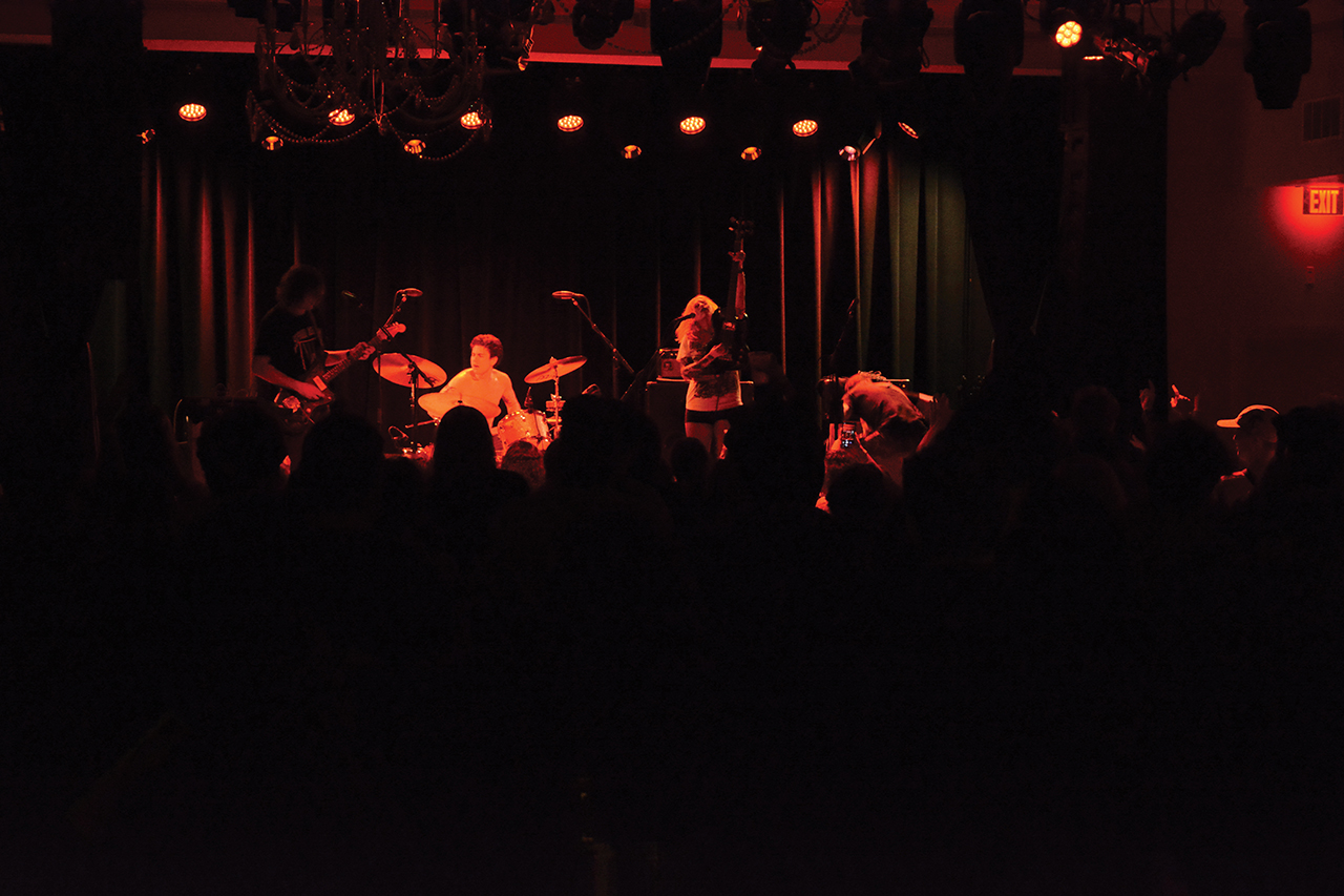 This is a photo of Frankie and the Witch Fingers, a band, standing onstage, finishing their final song under red lights.